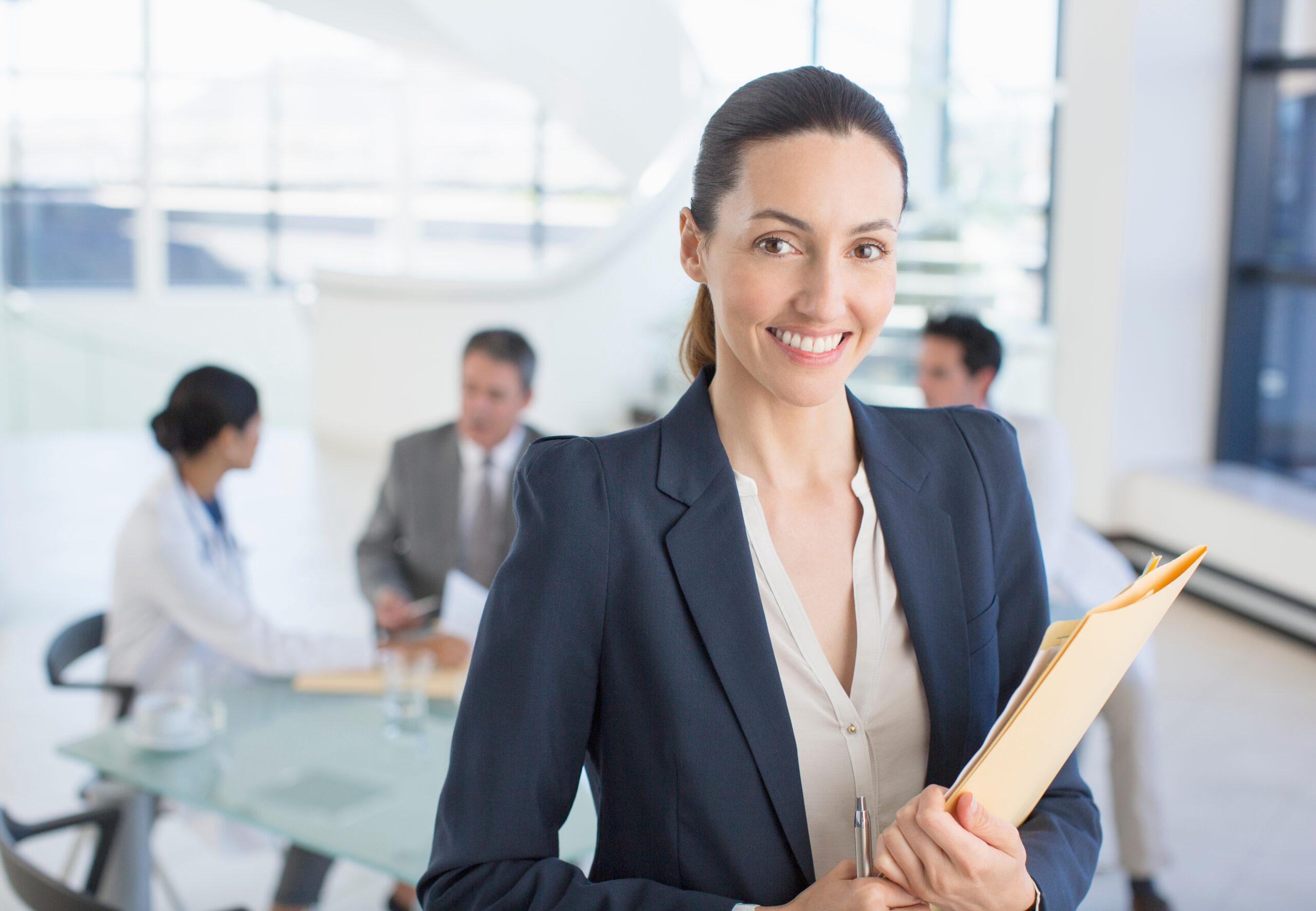 Portrait of smiling businesswoman in meeting with scientists in lab coats in background.