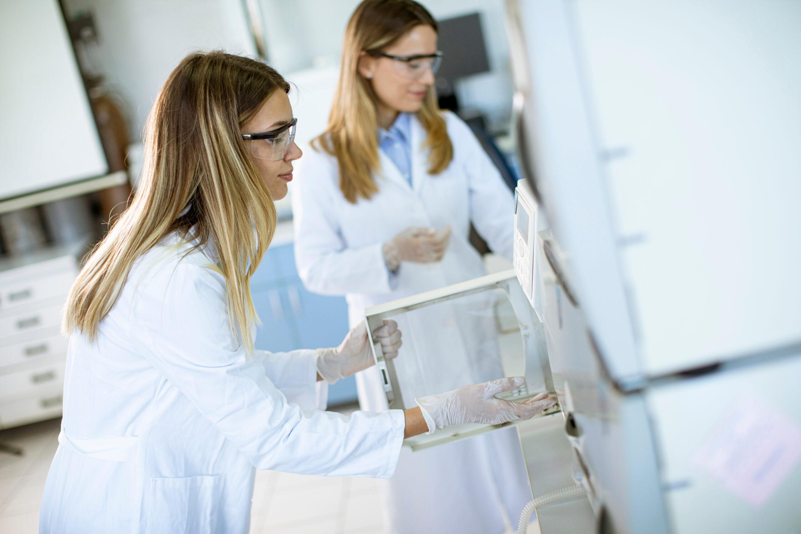 Female scientists in a white lab coat putting vial with a sample for an analysis on a ionchromatography system in biomedical lab